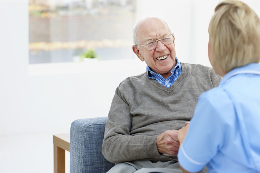 Happy elderly patient talking with nurse at home